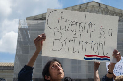 A demonstrator looks up at her sign (which reads "Citizenship is a Birthright") during a rally outside the Supreme court building demanding the court uphold the 14th Amendment to the U.S. Constitution.