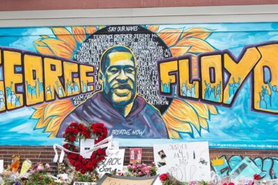 A mural with the image of George Floyd ihas flowers and signs protesting his murder lay beneath it five years later.