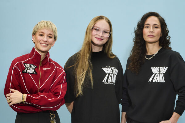 Megan Rapinoe, Becky Pepper Jackson, and Sue Bird stand together against a blue backdrop wearing "More Than A Game" apparel