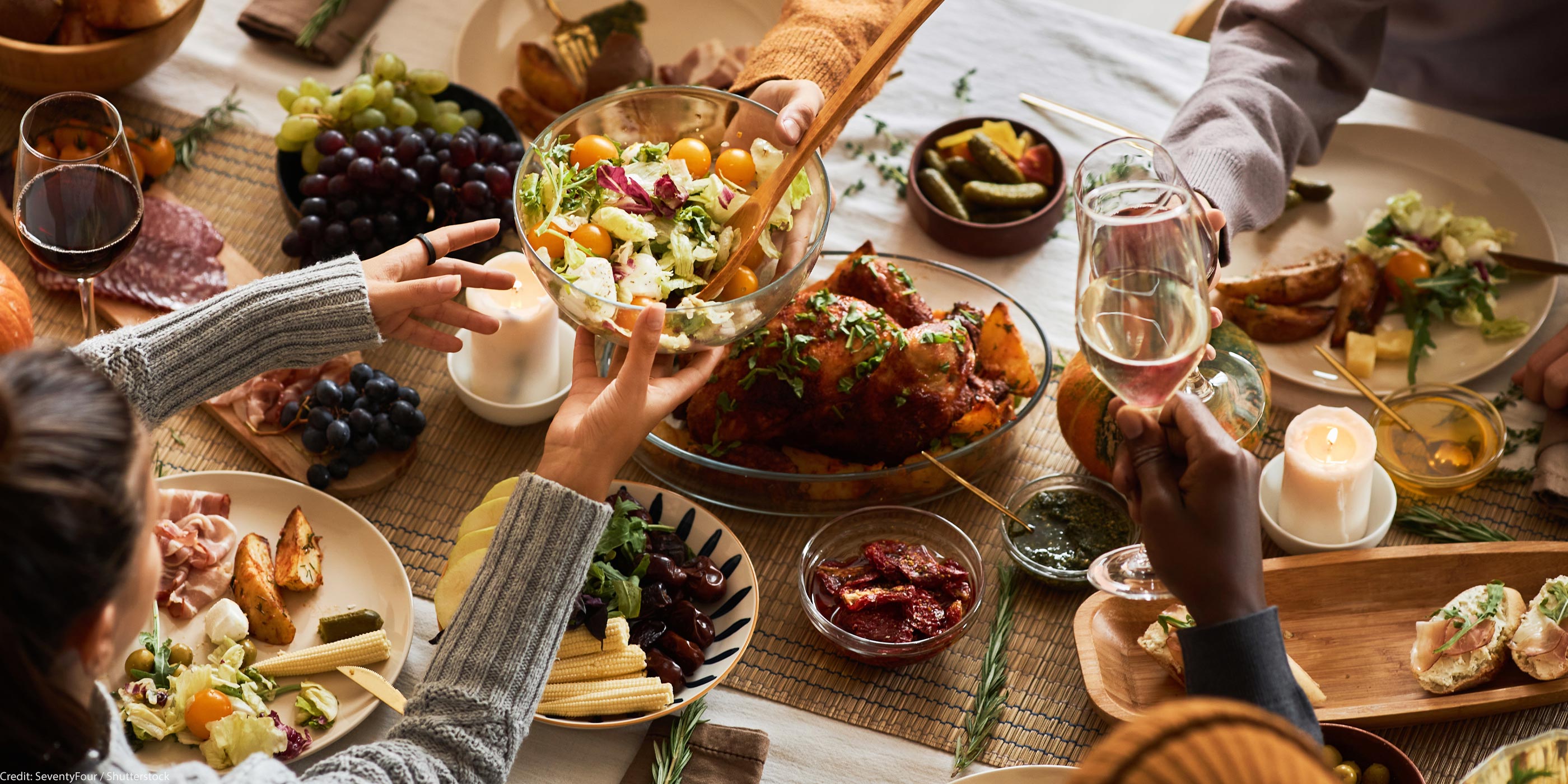 A multi-ethnic group of people sharing a festive, communal meal at a dining table with roasted chicken, salad, bread, fruit, and wine.