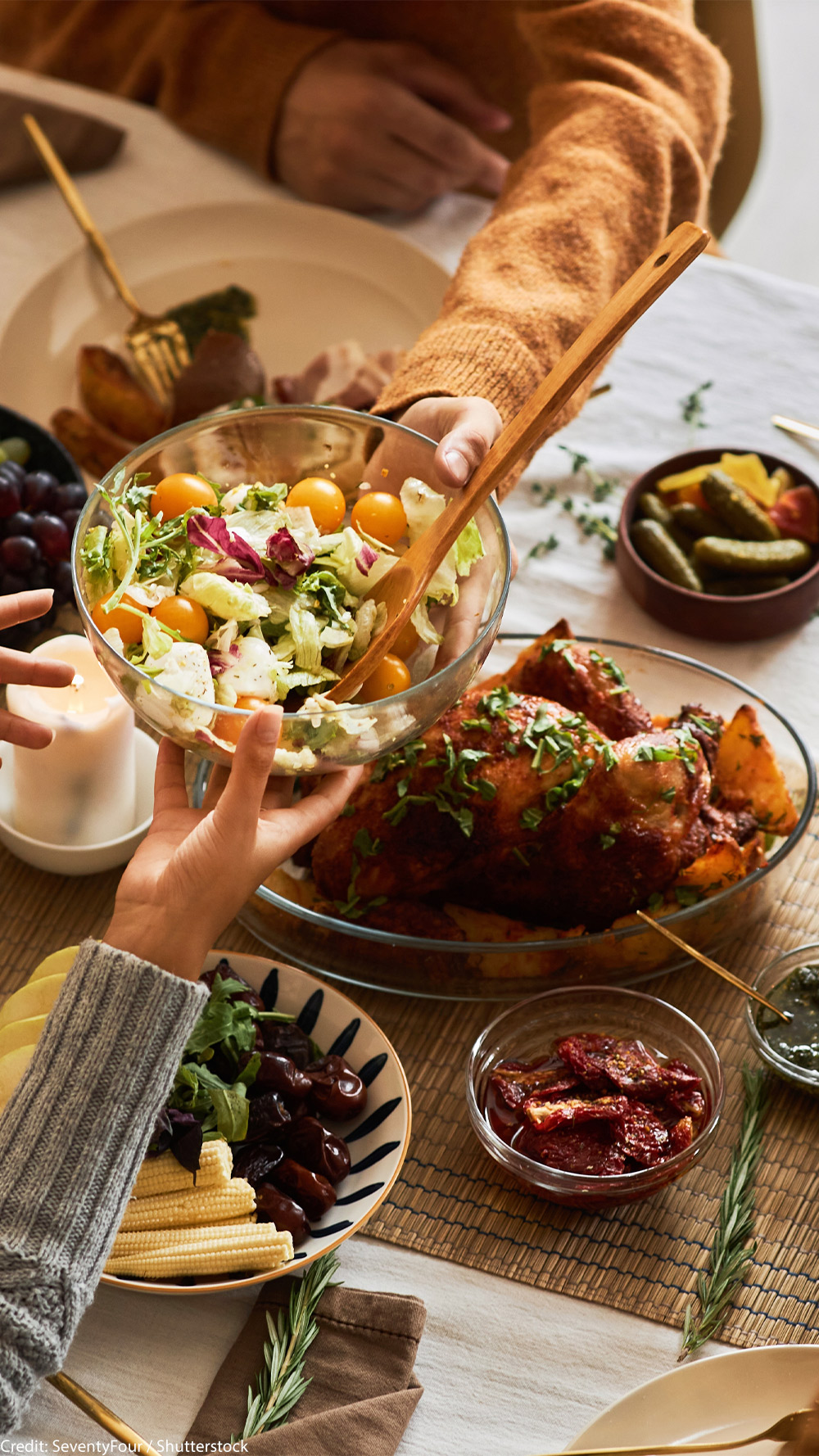 A multi-ethnic group of people sharing a festive, communal meal at a dining table with roasted chicken, salad, bread, fruit, and wine.