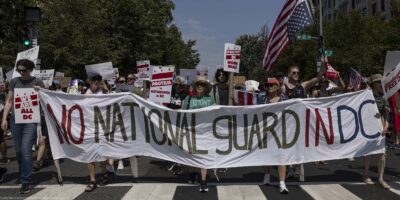 Demonstrators march in Washington, DC carrying a banner that reads " NO NATIONAL GUARD IN DC".