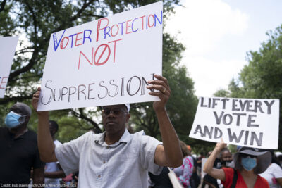 An individual at a demonstration, holding a sign that says "Voter Protection, Not Suppression."